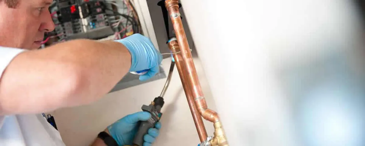 Water heater repair technician testing copper pipe connections and controls in Denver, CO